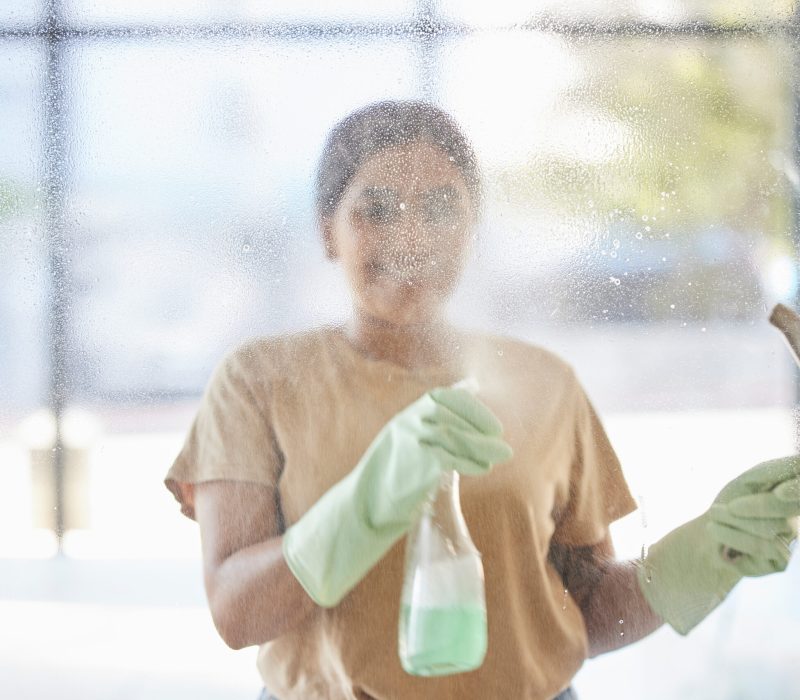 Happy, woman and cleaning window with smile, spray bottle and soap or detergent housekeeping in hom.