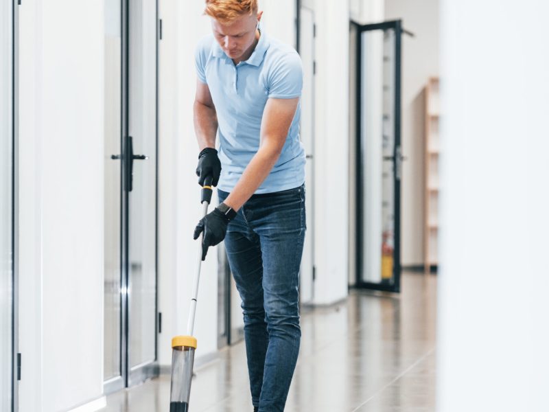 Young man works in the modern office. Uses vacuum cleaner.